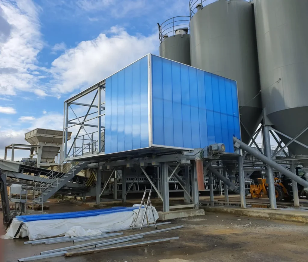 Cabine en cours d'habillage au pied de silos, panneaux de bardage bleus et profilés posés au sol